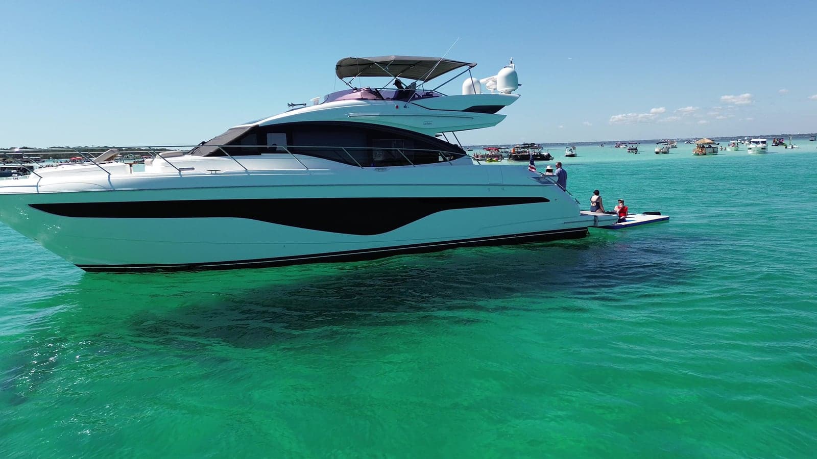 Side profile of the 62' Princess at anchor on clear green water, with her sportbridge and swim platform